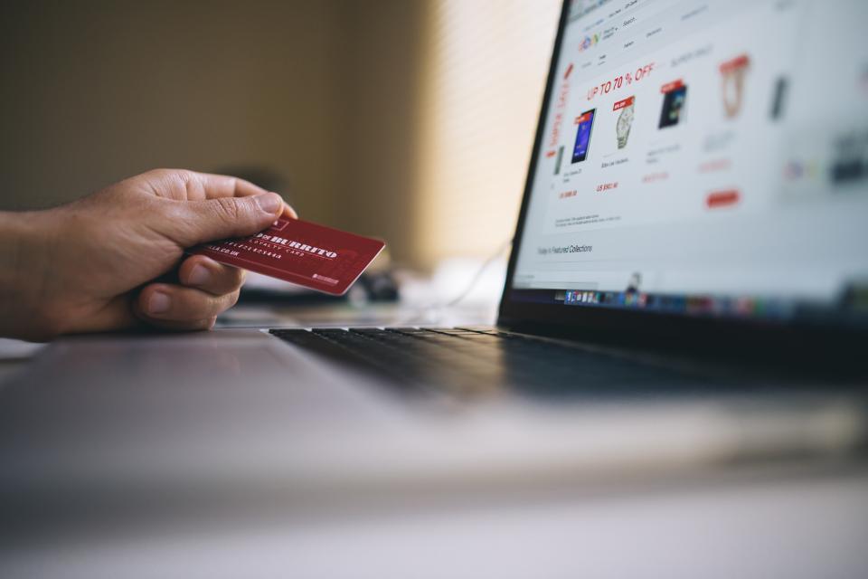 Hand holding a credit card in front of a laptop showing an online store